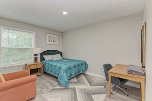 Un dormitorio con cama, escritorio, silla, mesita de noche, ventana con persianas e iluminación de pared.