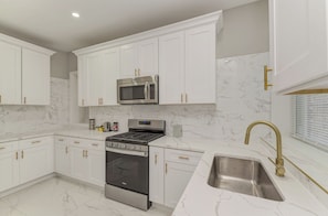 A modern kitchen with white cabinetry, a stainless steel microwave, a gas stove, and a sink with a gold faucet. - The Euclid House Stylish 6BR By UChicago, Obama Presidential Center & Lakefront (Chicago)