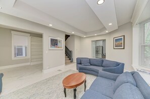 Un salón espacioso con un sofá azul, una mesa de centro de madera y una cocina al fondo.