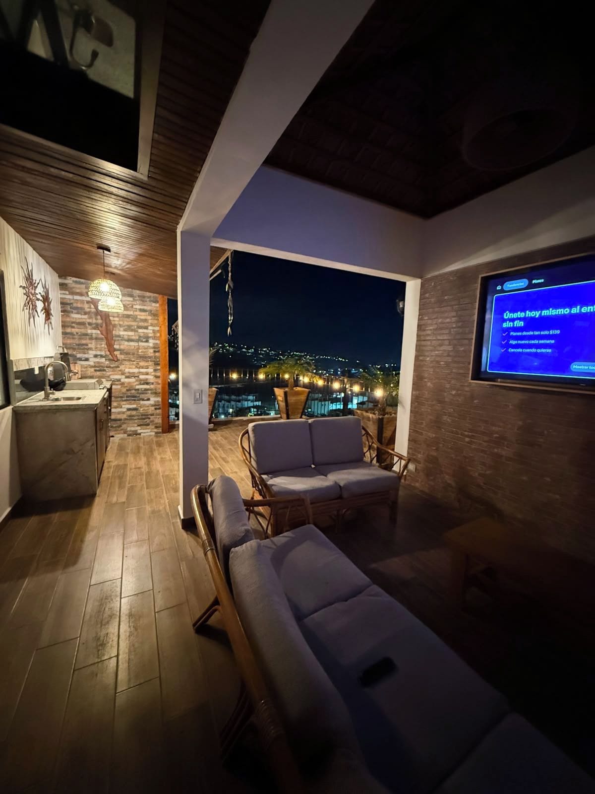 A modern living room with a view of a cityscape at night, a television screen, and a dining area with a table and chairs.