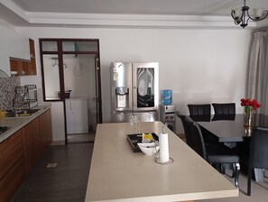 A modern kitchen with a central island, a refrigerator, and a dining area with chairs and a table. - Sleek and stunning 2 bedroom to let in kilimani, walking distance to yaya center (Nairobi)