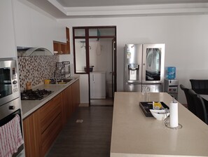 A modern kitchen with a gas stove, oven, and a built-in microwave. There is a refrigerator with a water dispenser and a freezer. The kitchen has wooden cabinets and a tiled backsplash. - Sleek and stunning 2 bedroom to let in kilimani, walking distance to yaya center (Nairobi)
