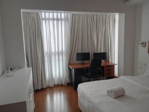 A hotel room with a bed, a desk with two monitors, a chair, and a window with curtains. - Sleek and stunning 2 bedroom to let in kilimani, walking distance to yaya center (Nairobi)