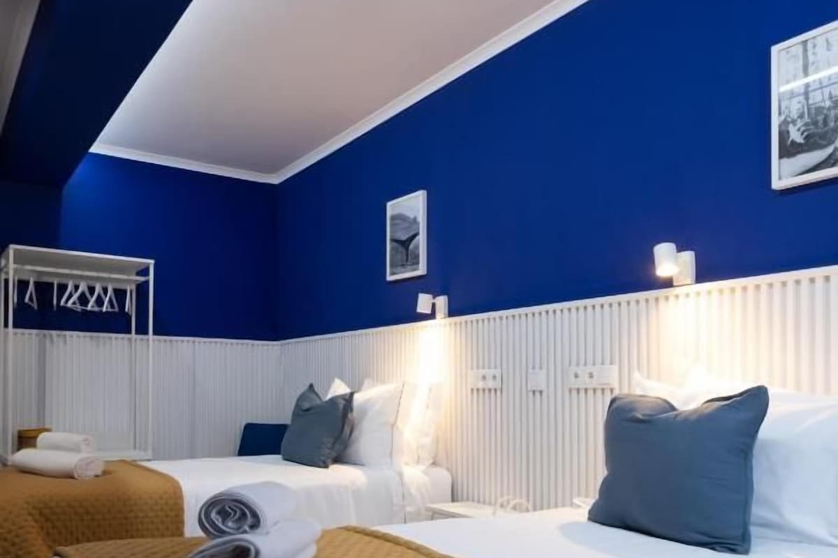 Habitación de hotel con dos camas, un radiador blanco y una pared azul.