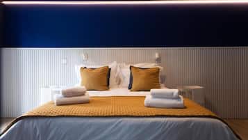 A hotel room with a bed, pillows, a bedside table, and a lamp.
