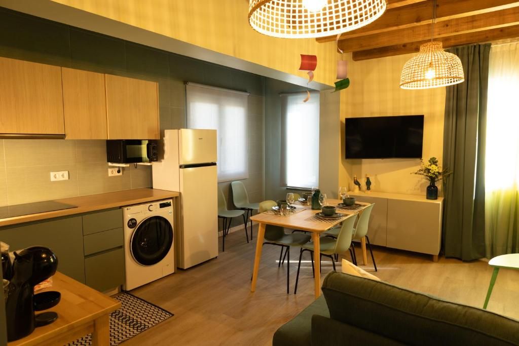 Cozinha compacta com micro-ondas, geladeira e máquina de lavar. Há uma área de refeições com mesa e cadeiras, e um sofá.