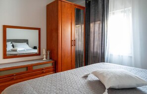 Ein Hotelzimmer mit Bett, Holzschrank, Spiegel und einem Fenster mit Vorhängen.