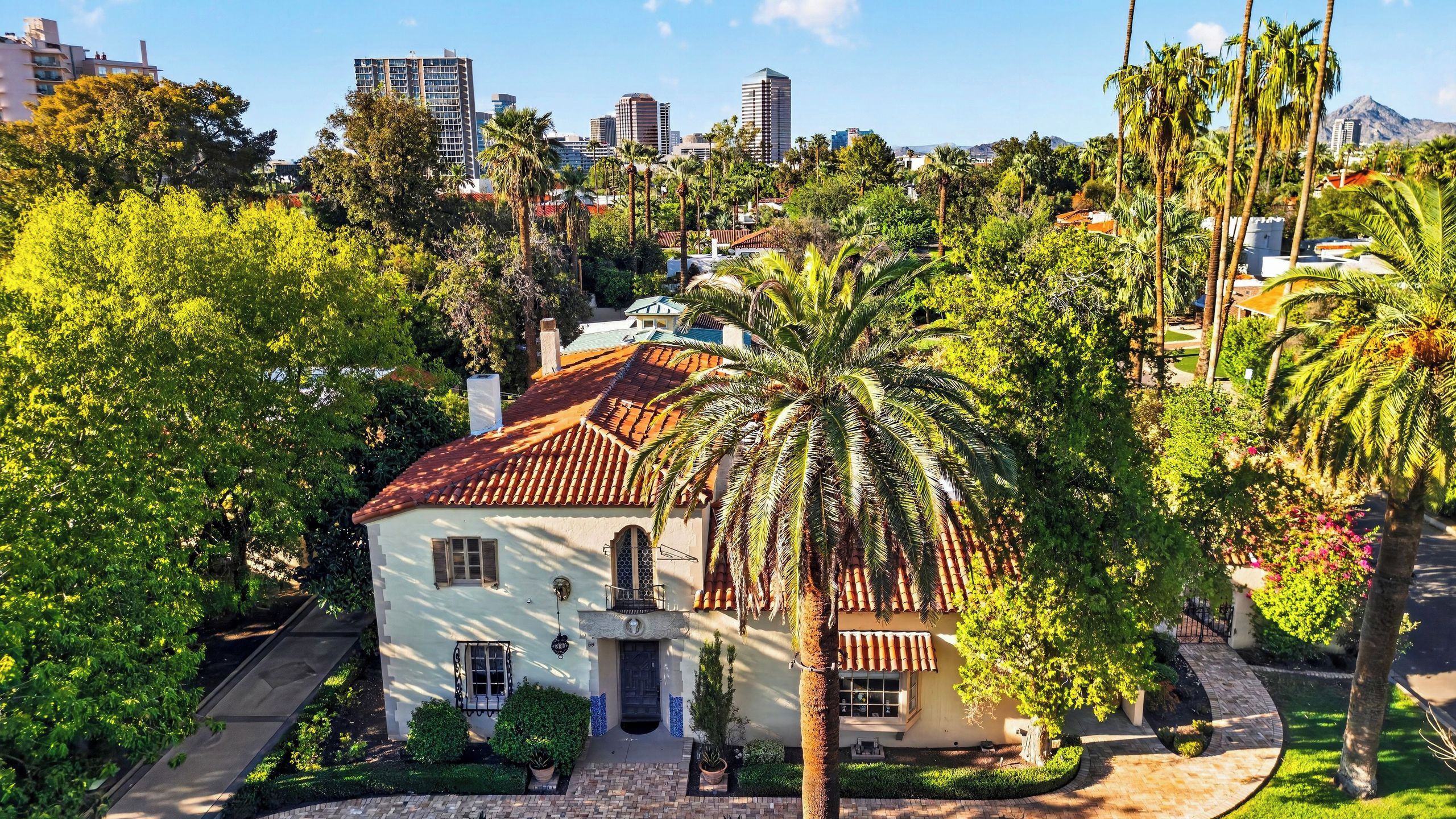 A white building with a red-tiled roof, surrounded by lush greenery and palm trees.