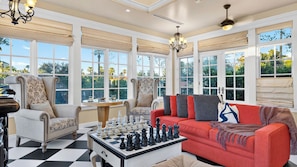 A spacious room with large windows, a chessboard, and a red sofa. - Palm Manor by Avantstay Historic Home + Private Pool Pergola Dining + Lawn Mins to Downtown (Phoenix)