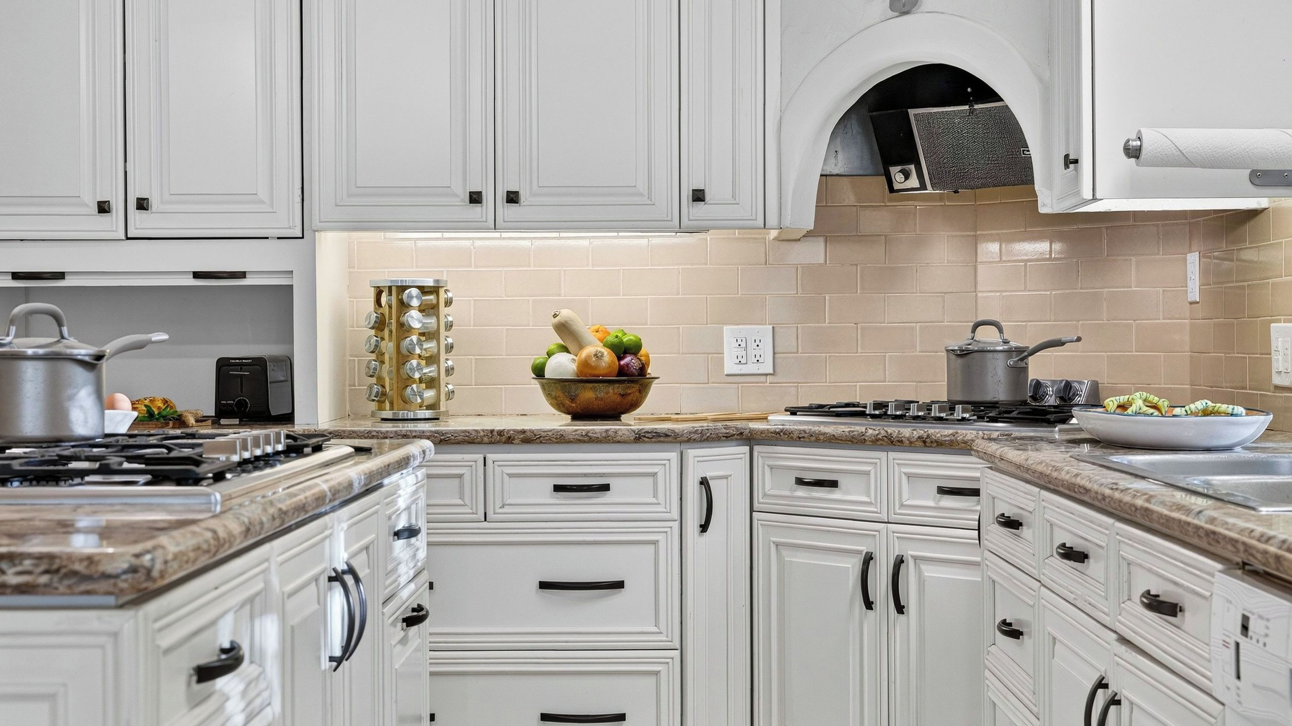 A modern kitchen with white cabinetry, a gas stove, a built-in oven, and a variety of kitchen appliances.