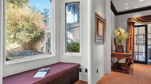 A room with a bench, a window with a view of a garden, and a door leading to another room. - Palm Manor by Avantstay Historic Home + Private Pool Pergola Dining + Lawn Mins to Downtown (Phoenix)