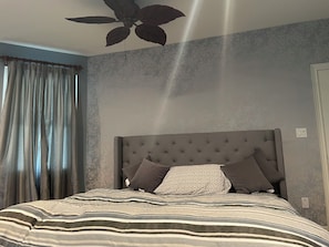 A bedroom with a tufted headboard, striped bedding, and a ceiling fan.