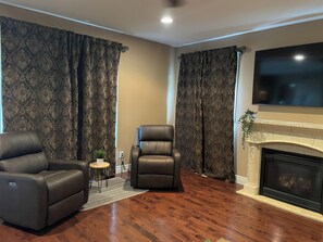 A living room with a fireplace, leather armchairs, and a television.