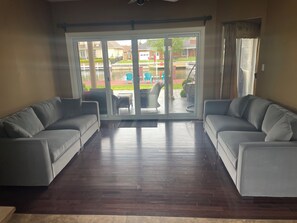 A room with two grey sofas, a wooden floor, and a sliding glass door leading to an outdoor patio with a table and chairs.