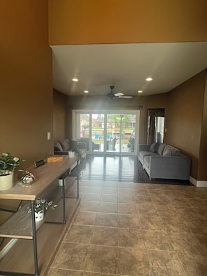 A spacious living area with a sofa, a coffee table, and a dining table with chairs. There is a sliding glass door leading to an outdoor area with chairs and a table.