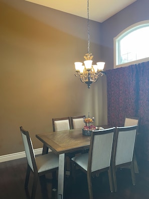 A dining area with a chandelier, a table with chairs, and a window with curtains.
