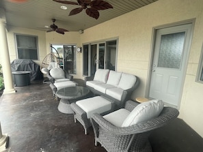 A covered patio area with wicker furniture, a ceiling fan, and a sliding glass door.