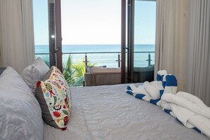 Une chambre avec un grand lit, une vue sur la mer et un balcon équipé d’une chaise.