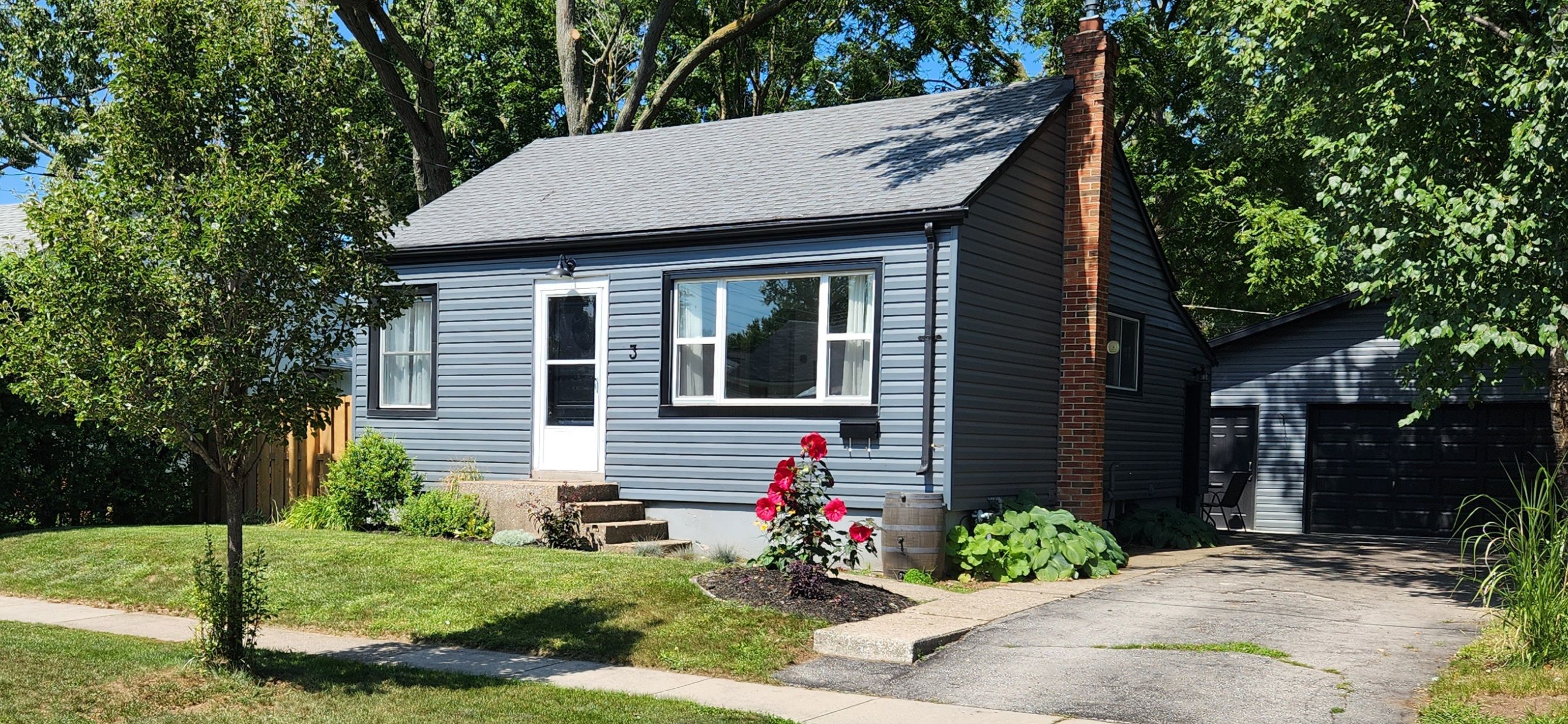 A two-story house with a grey exterior, a front porch, and a small garden with red flowers.