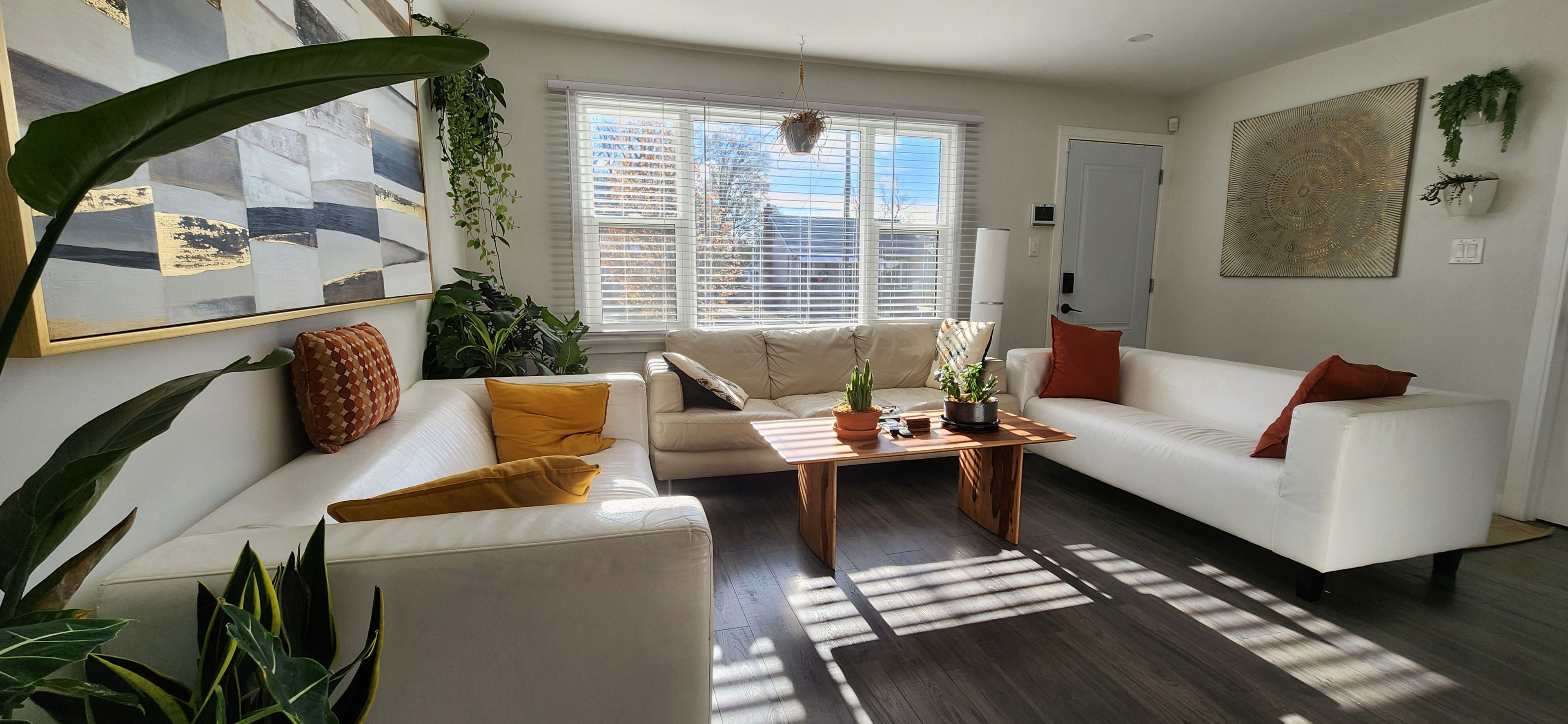 A modern living room with a white sofa, a wooden coffee table, and a large window with blinds.