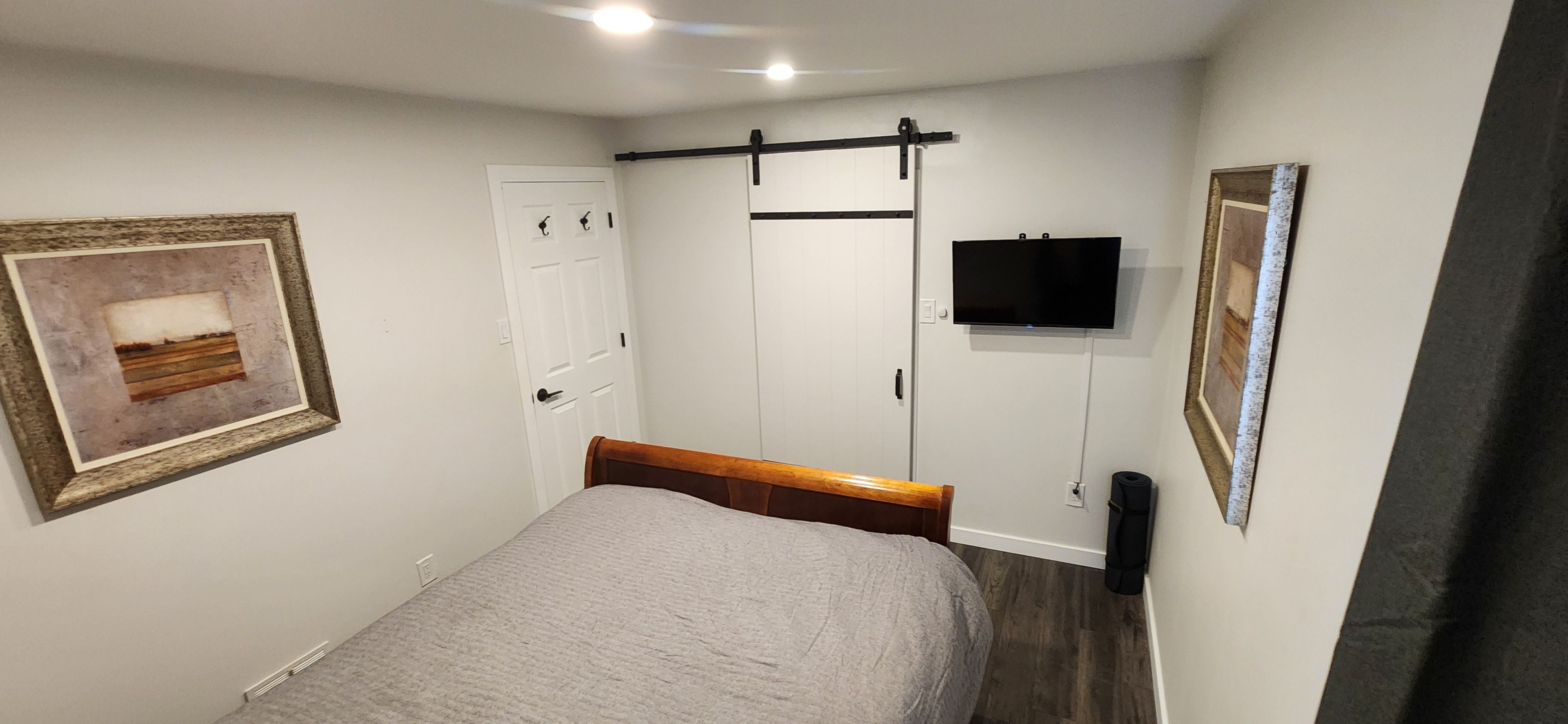 A bedroom with a bed, a door, a mounted TV, and a framed picture on the wall.