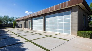 A modern building with large garage doors, a concrete driveway with grass inlays, and a clear blue sky. - Exeter House by Avantstay Sleeps 18 + Casita Pool + Spa + Theater Camelback Views (Phoenix)