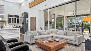 A modern living room with a sectional sofa, a coffee table, and a kitchen area with a large window. - Exeter House by Avantstay Sleeps 18 + Casita Pool + Spa + Theater Camelback Views (Phoenix)