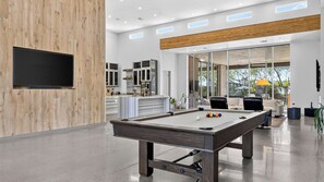 A modern indoor pool table with a wooden finish, a flat-screen TV mounted on a wooden wall, and a kitchen area with cabinets and a countertop. - Exeter House by Avantstay Sleeps 18 + Casita Pool + Spa + Theater Camelback Views (Phoenix)