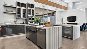A modern kitchen with a central island, built-in appliances, and a large window providing natural light. - Exeter House by Avantstay Sleeps 18 + Casita Pool + Spa + Theater Camelback Views (Phoenix)