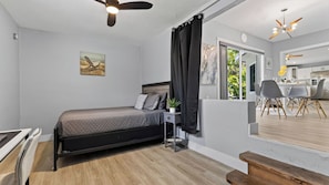A modern bedroom with a bed, bedside table, and a view of the kitchen. - Lauderdale Oasis by Avantstay 3-min Walk To Beach Hot Tub + Private Yard Near Las Olas (Fort Lauderdale)