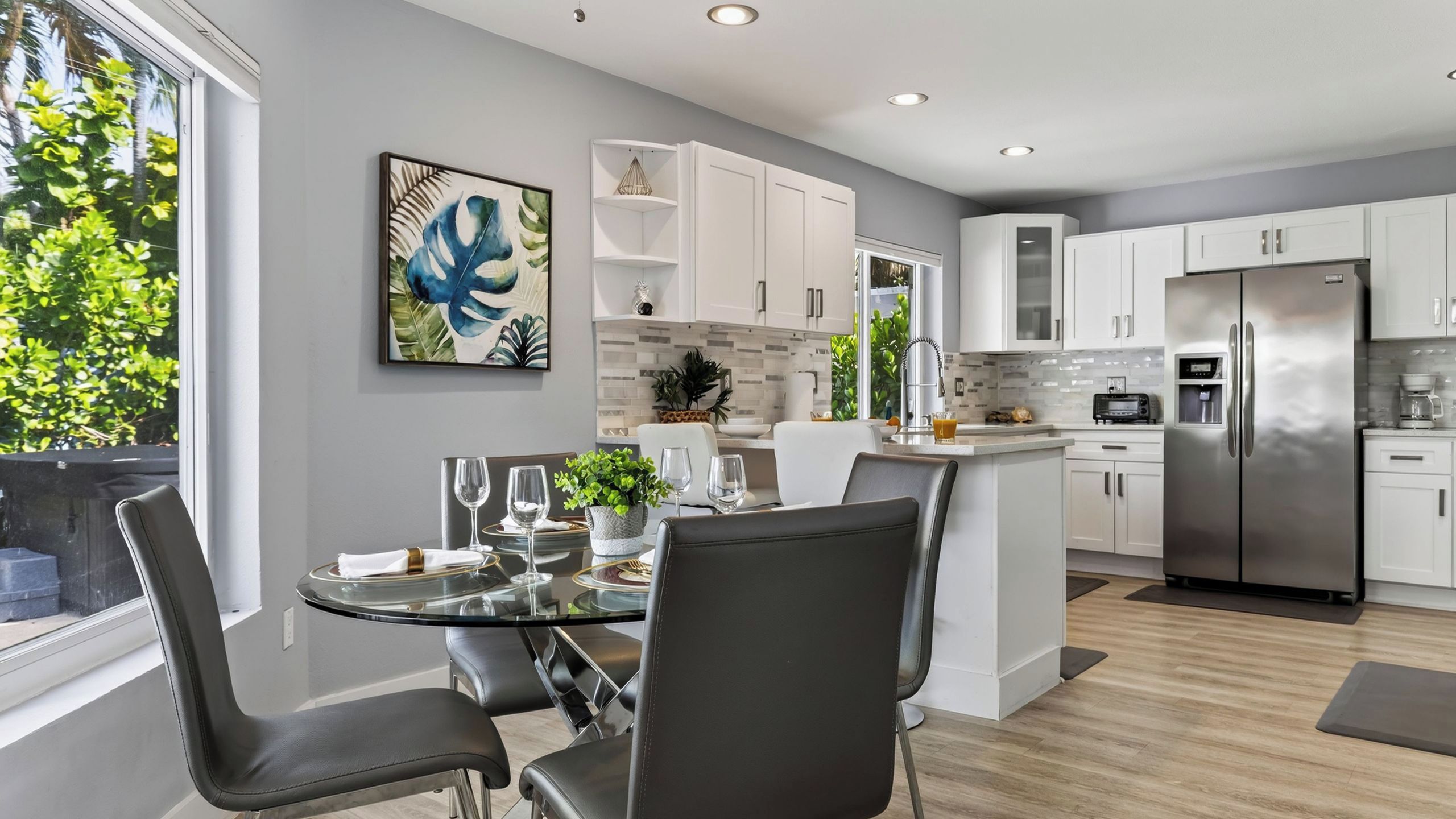 A modern kitchen with white cabinets, a stainless steel refrigerator, and a dining area with a glass table and chairs.