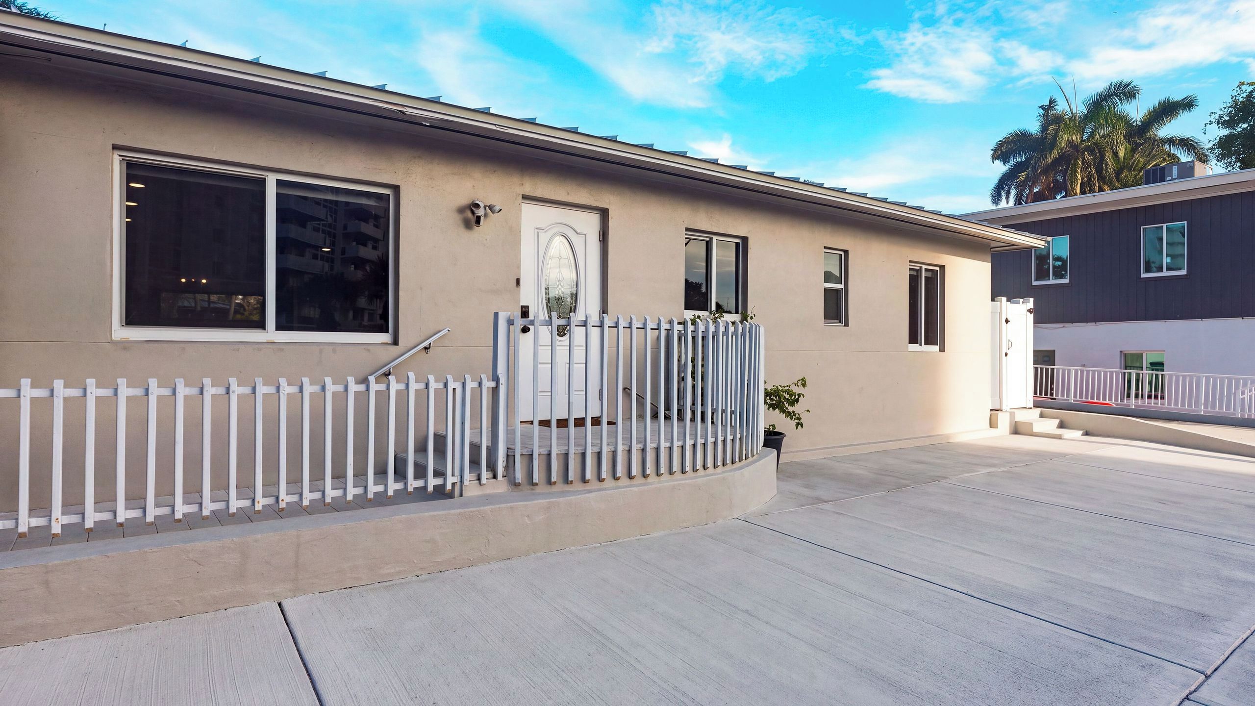 A residential building with a beige facade, a white front door, and a white picket fence.