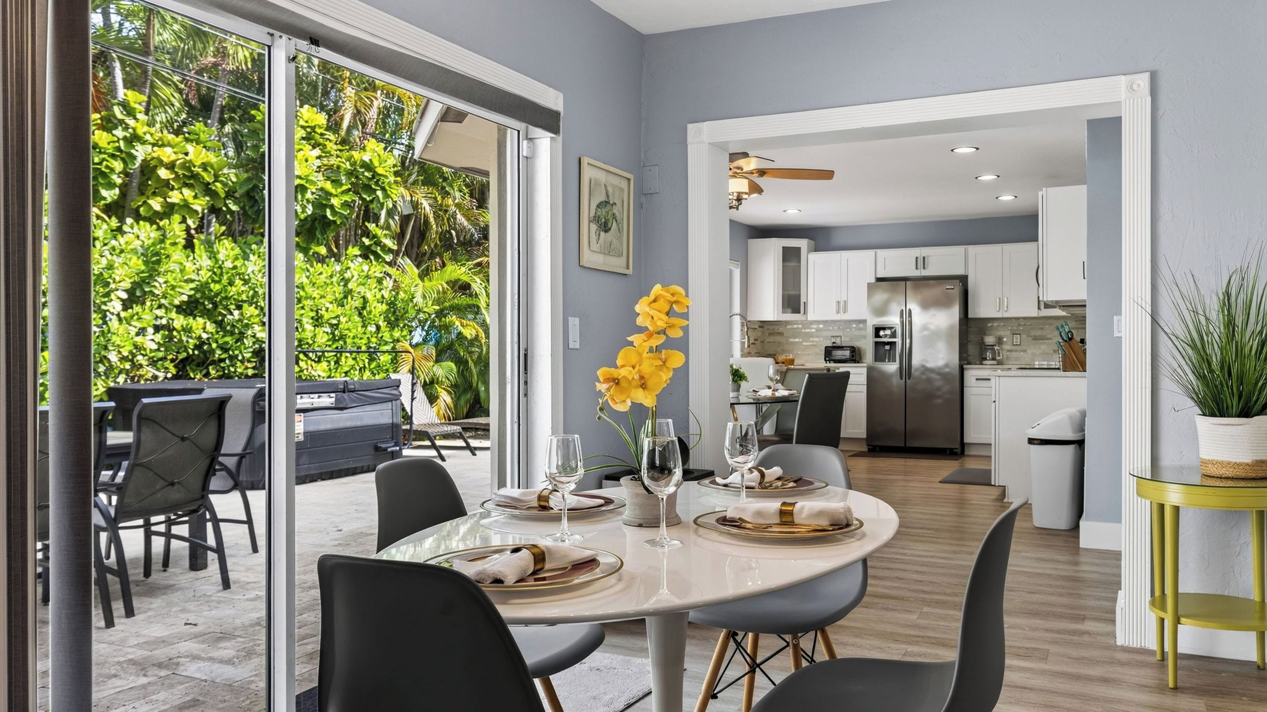 A modern dining area with a glass table, chairs, and a vase of yellow flowers.