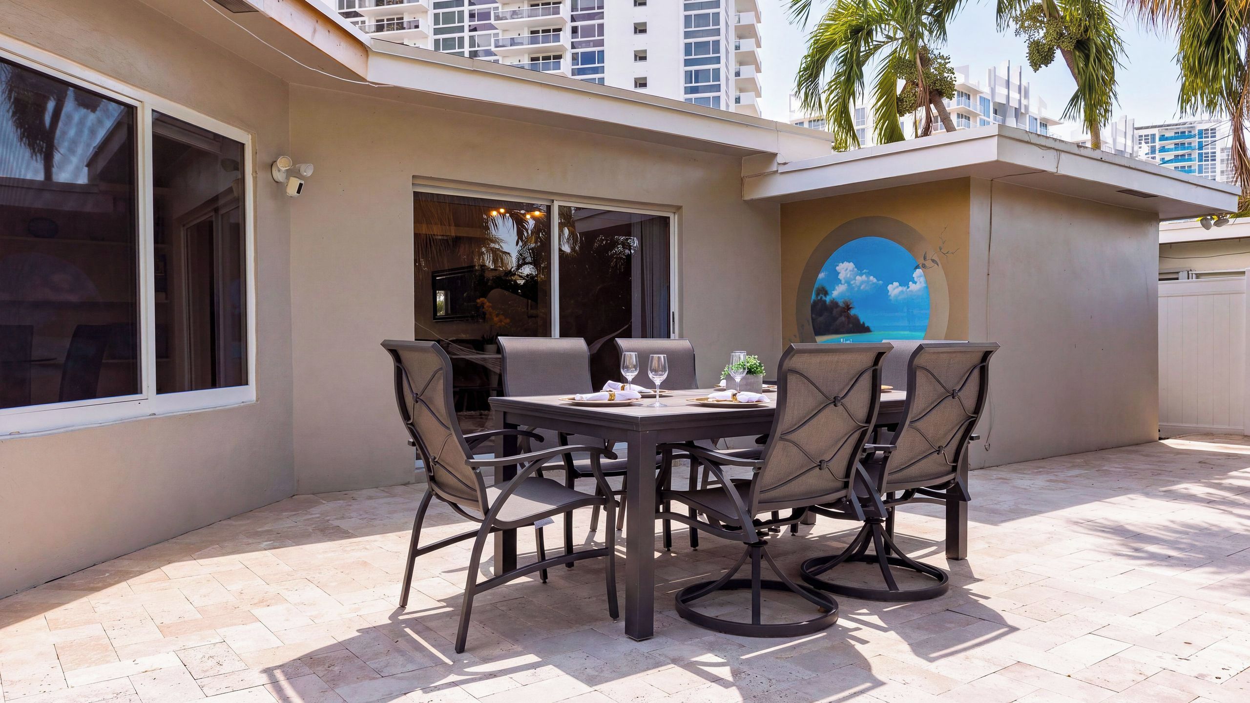 Um pátio externo com mesa e cadeiras, uma janela grande e vista para um edifício.