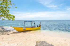 A yellow boat with a blue canopy on a sandy beach with clear water and a tree in the foreground. - Aloki Wim 4 – A pasos de la Playa (Playa Chiquita)