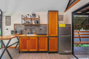 A compact kitchen with wooden cabinets, a stainless steel refrigerator, and a tiled backsplash. - Aloki Kalok 3 - Refugio cerca de la playa (Playa Chiquita)