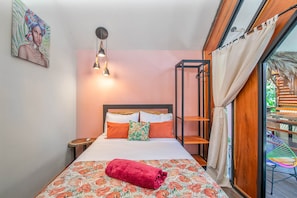 A hotel room with a bed, a nightstand, a hanging light fixture, a window with curtains, and a view of greenery outside. - Aloki Kalok 3 - Refugio cerca de la playa (Playa Chiquita)