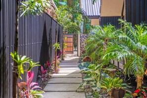 A narrow pathway flanked by lush tropical plants and a wooden gate leading to a building with a corrugated metal roof. - Aloki Villa – Sleeps 21 | Perfect for Friends & Families (Playa Chiquita)