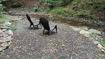 A paved area with two chairs and a small table, surrounded by rocks and a stream.