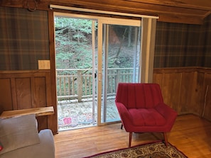 A wooden interior with a red chair, a bench, and a sliding glass door leading to a wooden deck.