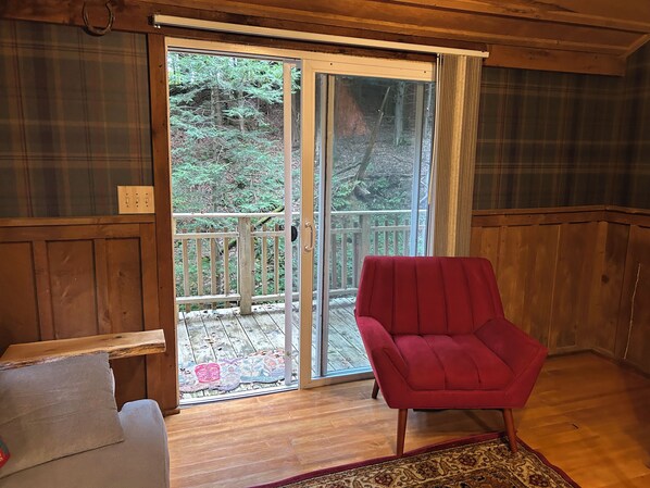 A wooden interior with a red chair, a bench, and a sliding glass door leading to a wooden deck.