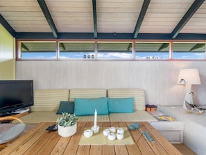 A cozy living room with a wooden ceiling, a sofa with teal cushions, a television, a table with a plant, candles, and knitting materials. - "Anita" - 400m from the sea by Interhome (Bindslev)