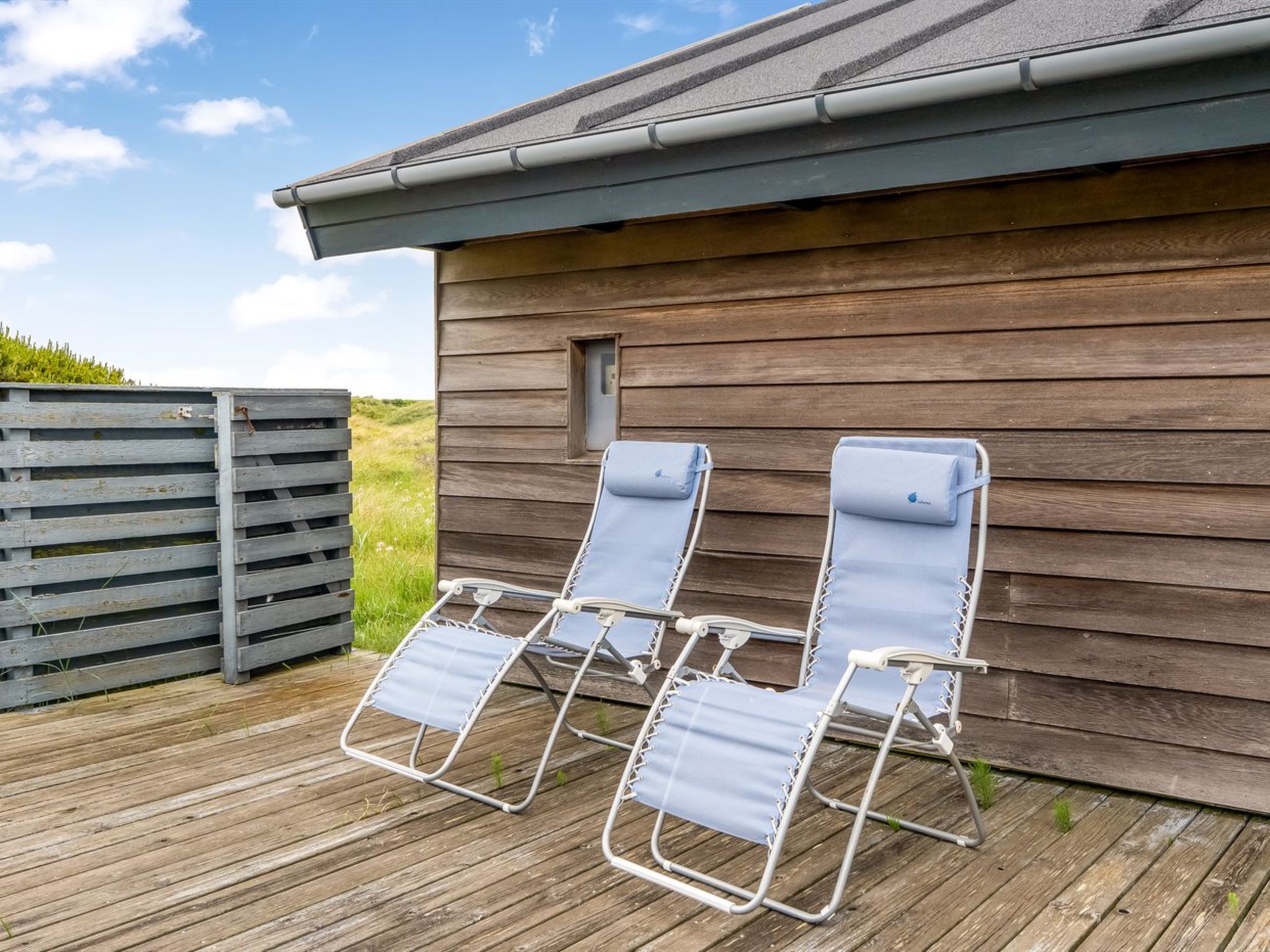 A wooden deck with two lounge chairs and a wooden building in the background.