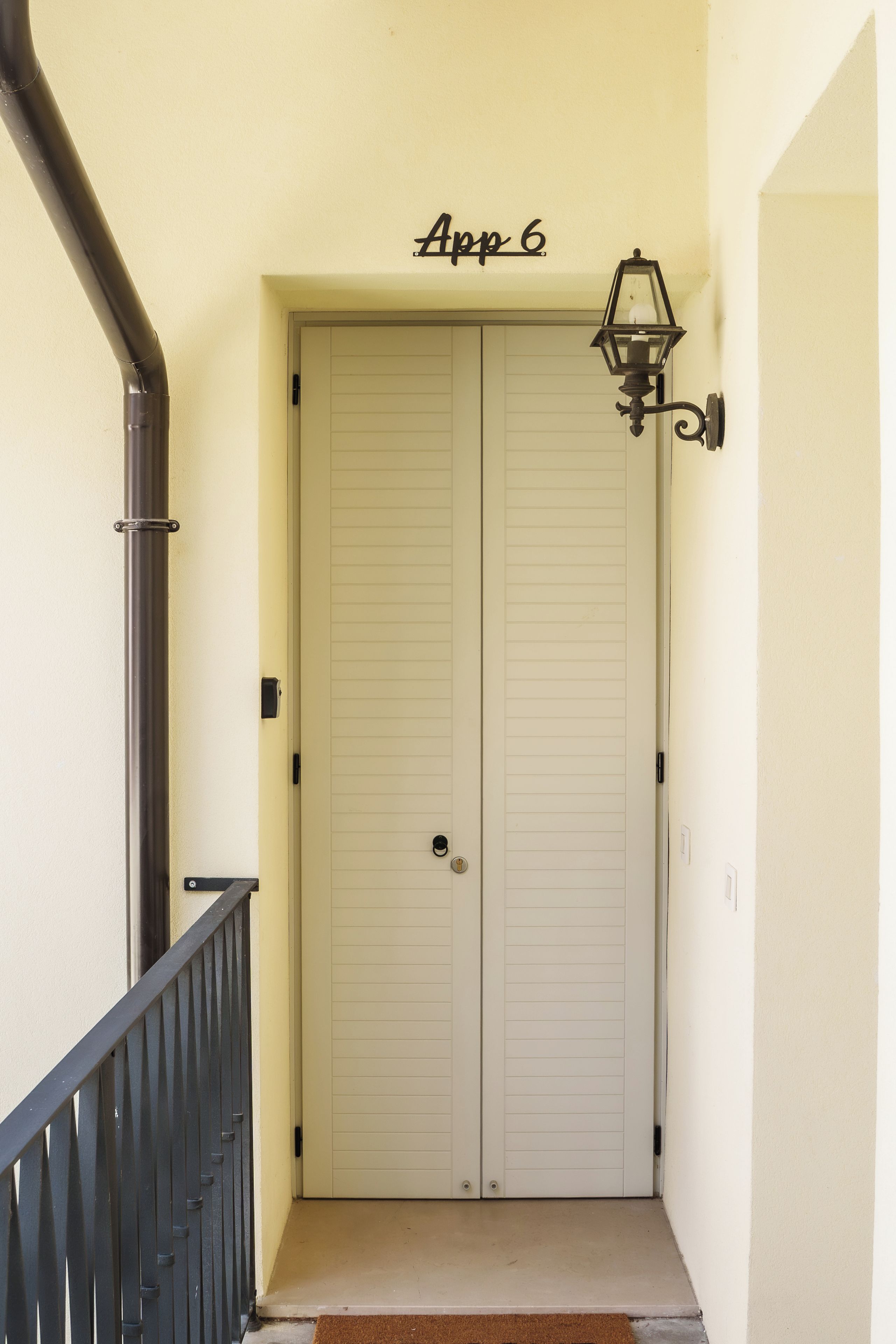 A double door with a doormat and a wall-mounted light fixture above it.