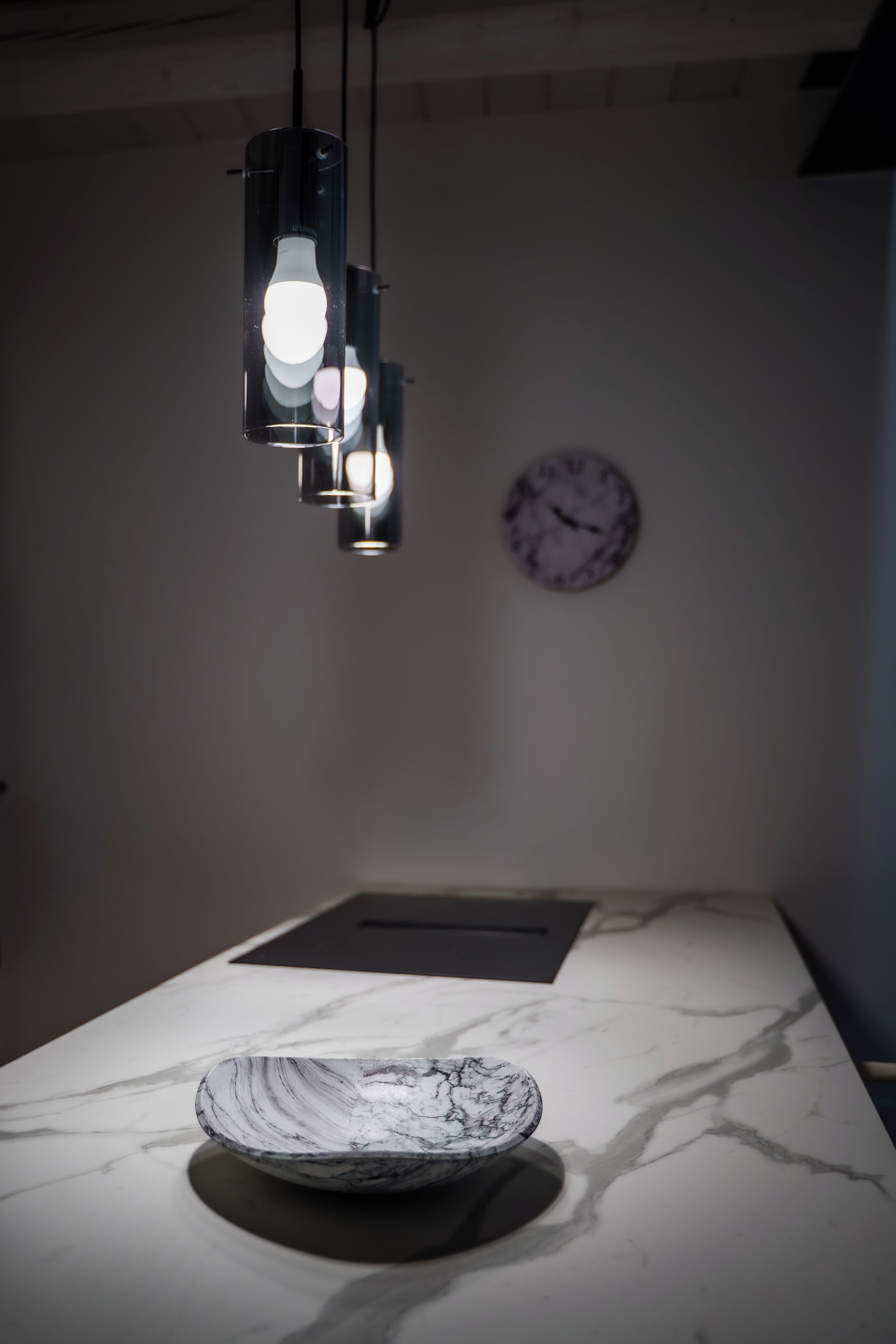 En bordplade i marmor med en skål, et vægur og hængende lamper.