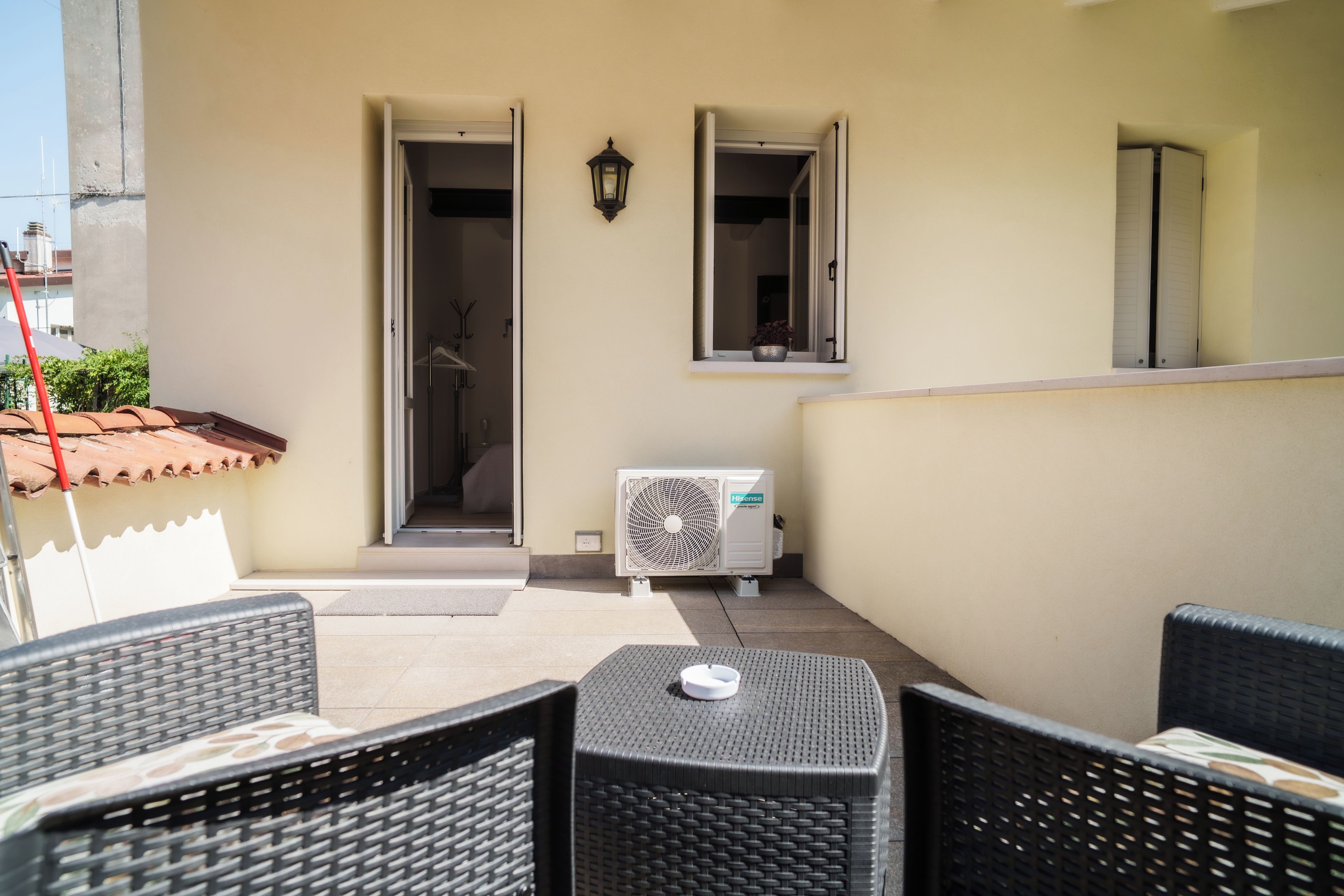Un área de estar al aire libre con muebles de mimbre, un aire acondicionado Hisense y vistas al interior del edificio de al lado.