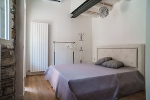 Een slaapkamer met een bed, een kapstok, een hanglamp en een stenen muur.