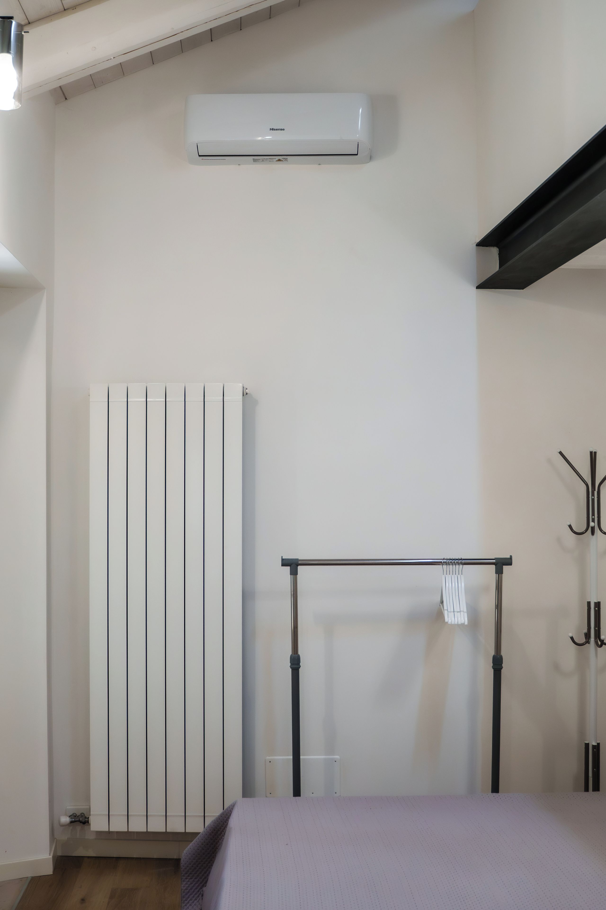 Et soveværelse med seng, radiator, klimaanlæg og knagerække.