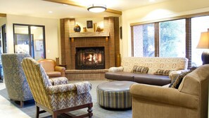 A cozy living room with a fireplace, comfortable seating, and a large window with blinds.