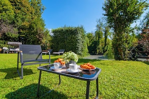 Een terras met zitplaatsen, een gedekte tafel, stoelen en uitzicht op een tuin.